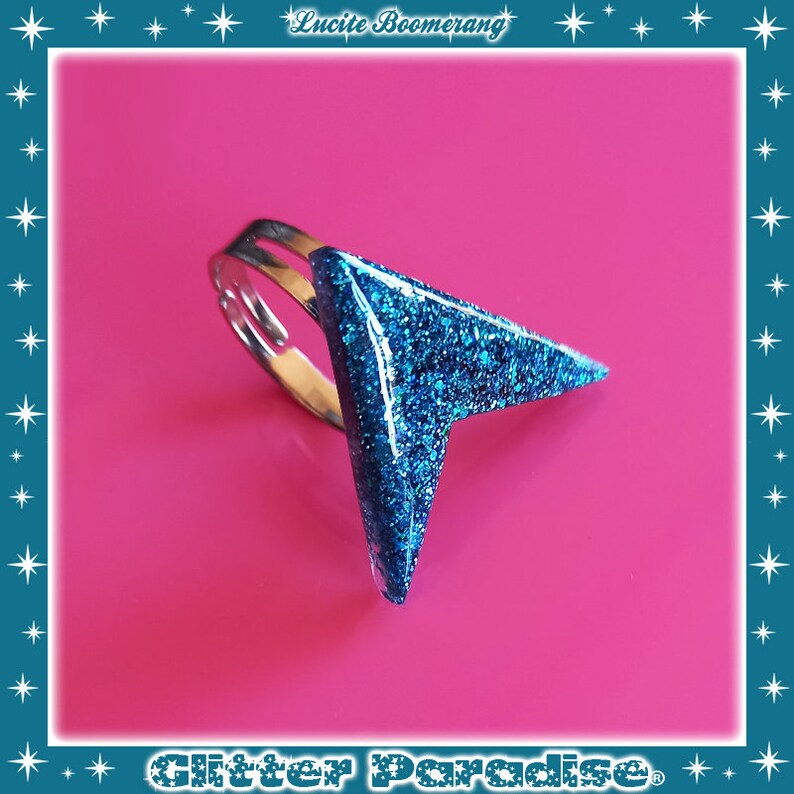 May include: A blue glitter ring with a pointed arrow shape. The ring is made of metal and has a silver finish.