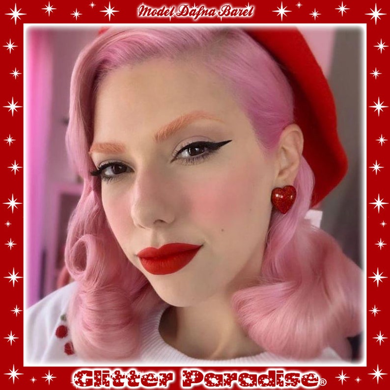 May include: A woman with pink hair and red lipstick is wearing a red beret and heart-shaped earrings. The earrings are red with glitter. The text "Glitter Paradise" is visible at the bottom of the image.