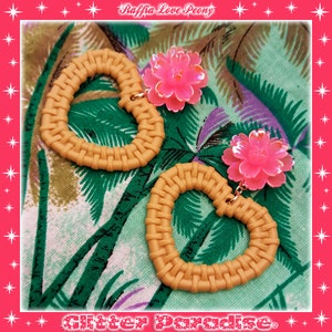 May include: A pair of heart-shaped earrings with a woven texture and pink flower charms. The earrings are on a tropical print fabric background. The text "Raffia Love Peony" and "Glitter Paradise" are visible in the image.