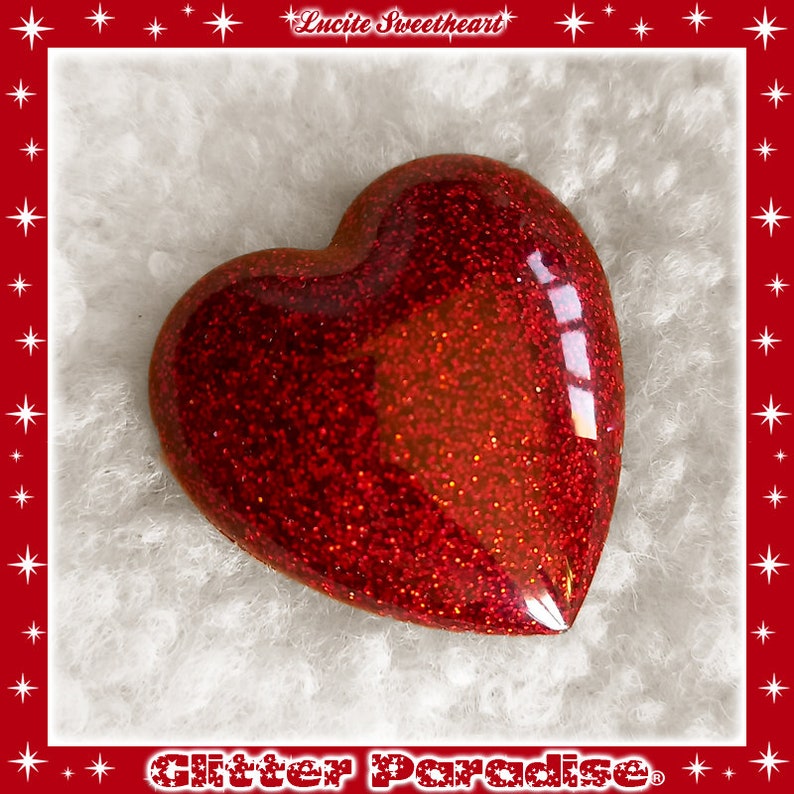 May include: A red glitter heart-shaped resin charm. The charm is shiny and has a slightly textured surface.