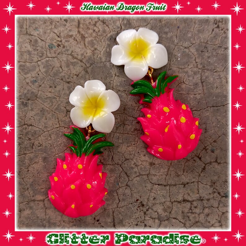 May include: A pair of dangle earrings featuring a pink dragon fruit with yellow dots and a white plumeria flower. The earrings are made of plastic and have a gold-colored metal hook.