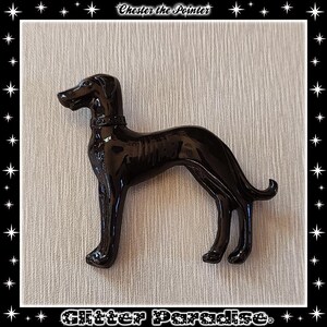 Op de afbeelding: Een glanzend zwart beeldje van een hond, waarschijnlijk een pointer, in profiel. De hond heeft een halsband en een gladde, gepolijste afwerking. De tekst "Chester the Pointer" staat bovenaan en "Glitter Paradise" onderaan.