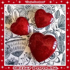 May include: Three red glitter heart-shaped ornaments on a black and white floral background. The text "Lucite Sweetheart" and "Glitter Paradise" are visible in the image.