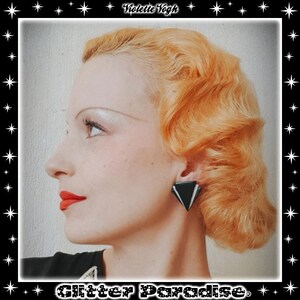 Peut inclure: Une femme aux cheveux blonds coiffés en un court bob bouclé, portant des boucles d'oreilles géométriques noires et blanches. La femme regarde sur le côté et porte du rouge à lèvres rouge.