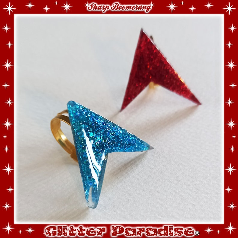 May include: Two glitter rings in the shape of a sharp boomerang. One ring is blue and the other is red.