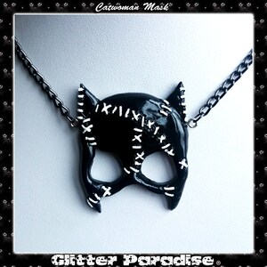 May include: Black catwoman mask necklace with white stitching detail. The mask is on a black chain.