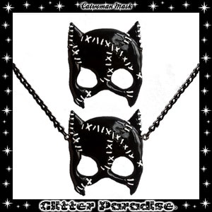 May include: Black catwoman mask necklace with a chain. The mask has white stitching details and is made of a shiny black material.