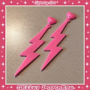 Puede incluir: Pendientes de rayo rosa brillante con tachuelas en forma de corazón. Los pendientes son de color rosa vibrante y tienen una textura brillante. Un accesorio divertido y de moda.