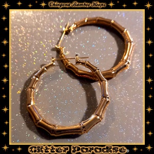 K&ouml;nnte beinhalten: Ein Paar goldfarbene Creolen mit einem strukturierten Bambus-Design. Die Ohrringe haben eine kreisf&ouml;rmige Form mit einem segmentierten Aussehen, das an Bambusstangen erinnert. Der Text "Chingona Bamboo Hoops" und "Glitter Paradise" ist zu sehen.
