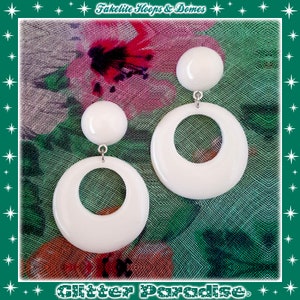 Puede incluir: Pendientes de aro blancos de baquelita con un gran diseño circular. Los pendientes cuelgan de un gancho plateado.