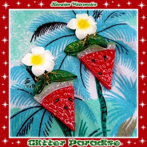 May include: A pair of watermelon slice earrings with a white plumeria flower charm. The earrings are made of red, green, and white resin and have a glossy finish.