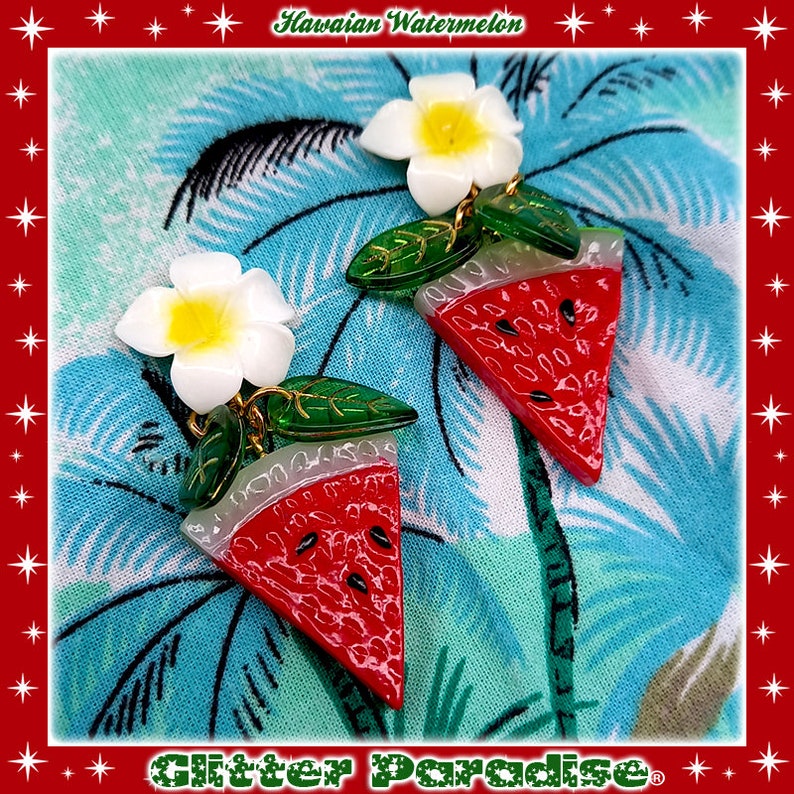 May include: A pair of watermelon slice earrings with a white plumeria flower charm. The earrings are made of red, green, and white resin and have a glossy finish.