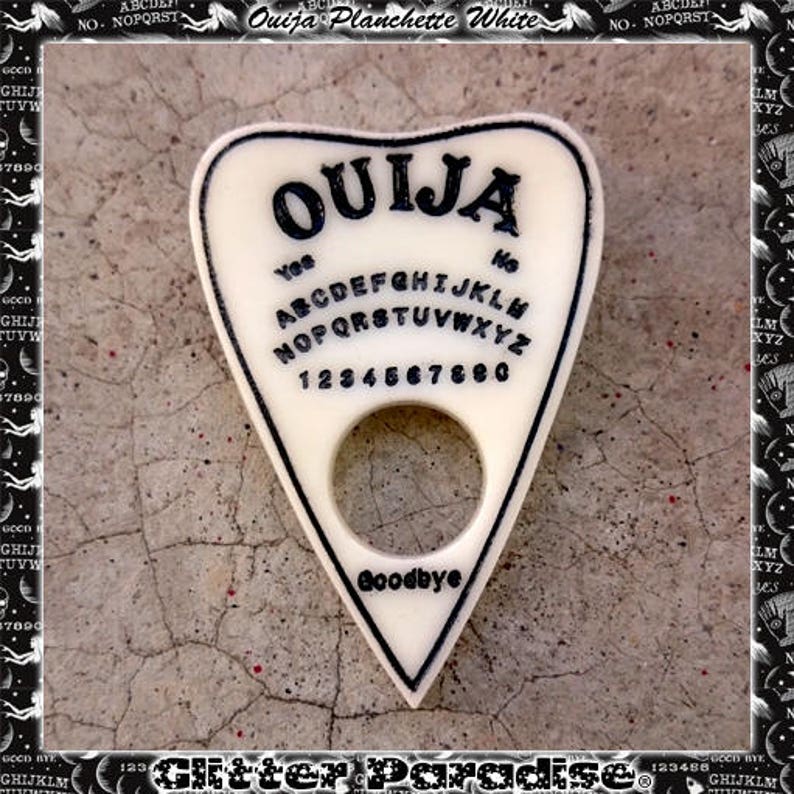 K&ouml;nnte beinhalten: Wei&szlig;e Ouija-Planchette aus Kunststoff mit schwarzem Rand und dem Wort "Ouija" in fetten schwarzen Buchstaben. Die Planchette hat ein Loch in der Mitte und die Buchstaben des Alphabets, die Zahlen 1-9 und 0 sowie die W&ouml;rter "Ja", "Nein" und "Auf Wiedersehen" sind in Schwarz gedruckt.