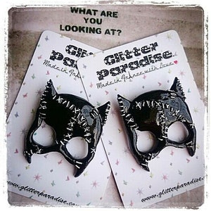 May include: Two black catwoman-style masks with stitched details on white cards with the text "Glitter Paradise" and "Made in France with Love".