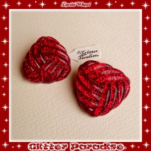 May include: A pair of red, sparkly, lucite earrings in a knotted design. The earrings are labeled "Glitter Paradise".