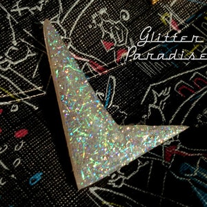 May include: A white, sparkly, triangular-shaped, glitter-covered, decorative piece. The piece is on a black background with white scribbles and the text "Glitter Paradise".