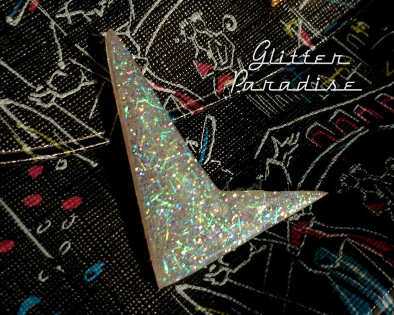 May include: A white, sparkly, triangular-shaped, glitter-covered, decorative piece. The piece is on a black background with white scribbles and the text "Glitter Paradise".