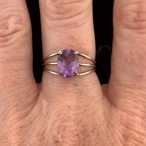 May include: A silver ring featuring a large, oval-cut amethyst gemstone. The ring has a triple-band design, with the gemstone securely set in the center. The amethyst displays a rich purple hue, adding a touch of elegance to the jewelry.