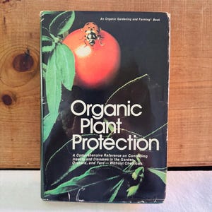 May include: A book titled "Organic Plant Protection" with a black cover. The cover features a red tomato with a ladybug and green leaves. The book is a comprehensive reference on controlling insects and diseases in the garden, orchard, and yard.