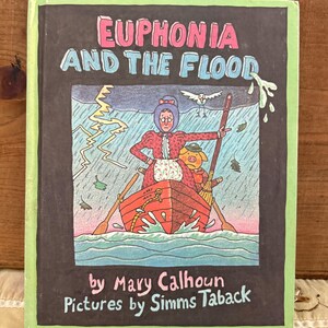 May include: A children's book titled "Euphonia and the Flood" with a green border. The cover illustration depicts a woman and a pig in a boat during a storm. The book's title is in pink and blue lettering.