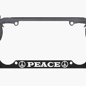 May include: Black license plate frame with palm tree accents and the word "PEACE" in white block letters. The peace symbol is incorporated into the design. The frame is designed to fit a standard license plate.
