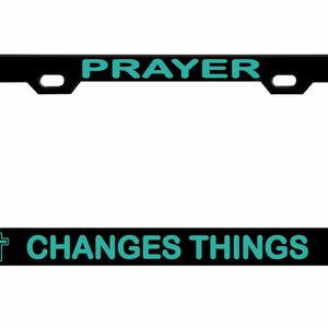 May include: Black license plate frame with the words "PRAYER" and "CHANGES THINGS" in teal lettering. Teal crosses are on each end of the bottom text. The frame is rectangular with rounded corners.