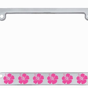 May include: A chrome license plate frame with palm tree accents on the corners. The bottom of the frame features a row of pink hibiscus flowers. The frame has four mounting holes.