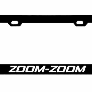 May include: Black license plate frame with the text "ZOOM-ZOOM" in white. The frame has a rectangular shape with rounded corners and two mounting holes at the top. The text is centered at the bottom.