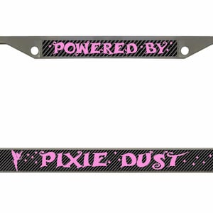 Könnte beinhalten: Ein silberner Kennzeichenrahmen mit schwarzem Carbonfaser-Hintergrund und rosa Schriftzug "Powered by Pixie Dust".