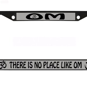 May include: Black license plate frame with a gray top and bottom border. The top border has the Om symbol and the word "OM". The bottom border reads "THERE IS NO PLACE LIKE OM" with the Om symbol on each side.