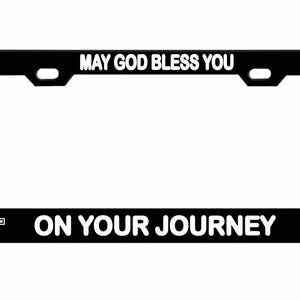 May include: Black license plate frame with white text that reads "MAY GOD BLESS YOU" at the top and "ON YOUR JOURNEY" at the bottom. White cross symbols are on each side of the bottom text. The frame has a rectangular shape.