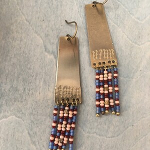 May include: A pair of long, rectangular earrings with a textured metal design and a fringe of blue, pink and red beads.