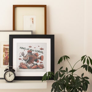 Peut inclure: Une impression encadrée en noir avec un fond blanc et une illustration colorée d'un poisson-lion avec le texte "KING of the CORAL!"