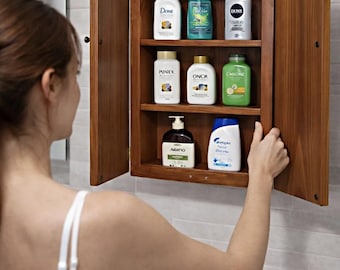 May include: A rectangular wooden wall-mounted cabinet with two hinged doors open to reveal three interior shelves. The shelves contain various personal care bottles including brands labeled Dove, Poniex, Onca, and others with assorted colored caps.