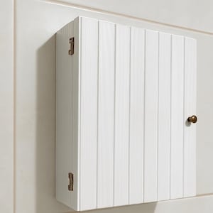 May include: A white wall-mounted cabinet featuring a vertical beadboard panel design on the front door. The cabinet includes two visible metallic hinges on the left side and a small, round metallic knob on the right side for opening the door.