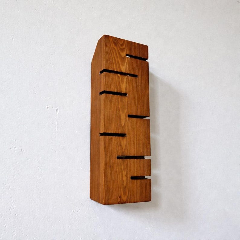 A vertical rectangular wooden wall sconce with warm LED light shining through carved horizontal openings. The wood has a natural grain and rustic brown finish. The style is minimalist, cozy, and modern, suitable for hallway, living room, or bedroom wall lighting.
