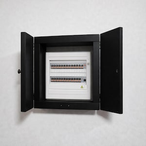 Puede incluir: Un armario de panel eléctrico negro con puertas abiertas, que revela un panel blanco con numerosos interruptores y luces indicadoras. El armario está montado en una pared blanca, proporcionando un aspecto limpio y moderno.