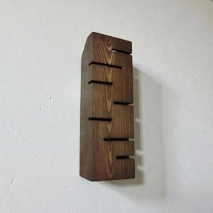 A vertical rectangular wooden wall sconce with warm LED light shining through carved horizontal openings. The wood has a natural grain and rustic brown finish. The style is minimalist, cozy, and modern, suitable for hallway, living room, or bedroom wall lighting.