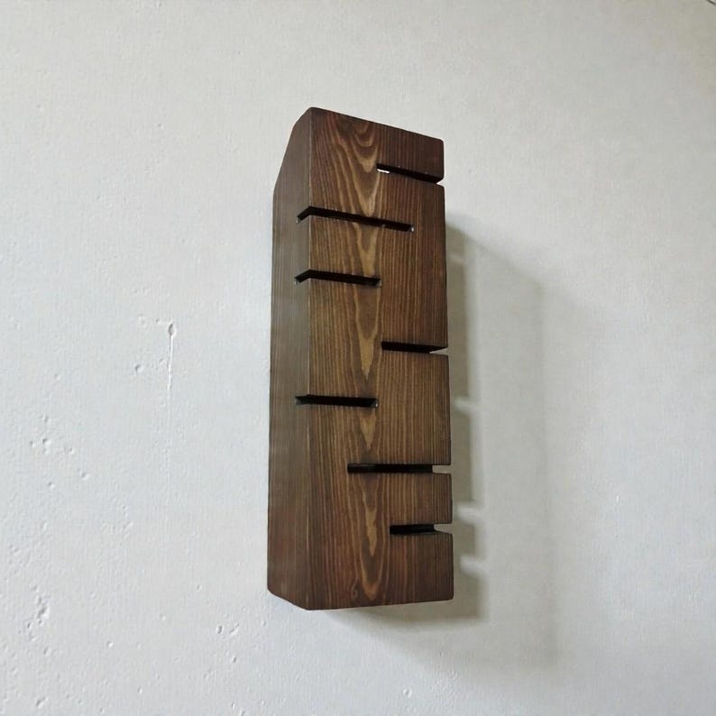 A vertical rectangular wooden wall sconce with warm LED light shining through carved horizontal openings. The wood has a natural grain and rustic brown finish. The style is minimalist, cozy, and modern, suitable for hallway, living room, or bedroom wall lighting.
