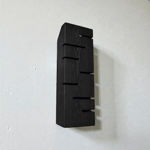 A vertical rectangular wooden wall sconce with warm LED light shining through carved horizontal openings. The wood has a natural grain and rustic brown finish. The style is minimalist, cozy, and modern, suitable for hallway, living room, or bedroom wall lighting.