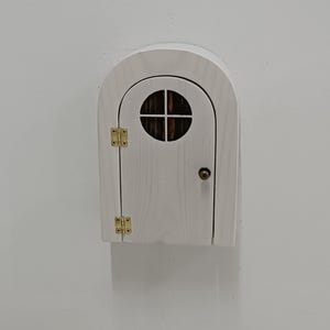 May include: White wooden door with a small round window and brass hinges. The door is arched at the top and has a small brass knob.