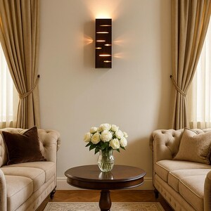 A vertical rectangular wooden wall sconce with warm LED light shining through carved horizontal openings. The wood has a natural grain and rustic brown finish. The style is minimalist, cozy, and modern, suitable for hallway, living room, or bedroom wall lighting.