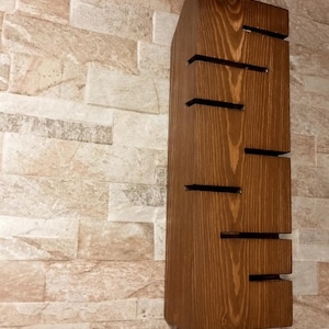 A vertical rectangular wooden wall sconce with warm LED light shining through carved horizontal openings. The wood has a natural grain and rustic brown finish. The style is minimalist, cozy, and modern, suitable for hallway, living room, or bedroom wall lighting.
