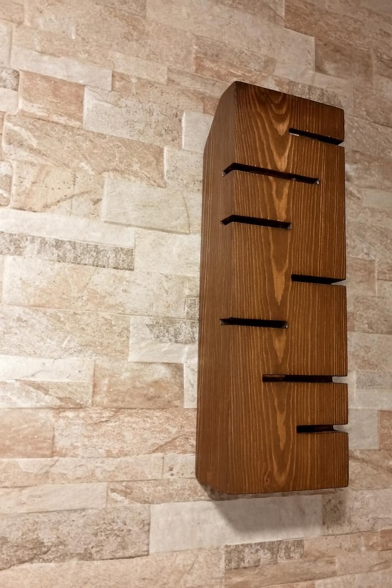 A vertical rectangular wooden wall sconce with warm LED light shining through carved horizontal openings. The wood has a natural grain and rustic brown finish. The style is minimalist, cozy, and modern, suitable for hallway, living room, or bedroom wall lighting.