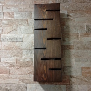 A rustic wooden wall sconce with warm glowing light. The lamp is carved with several horizontal slots that let the light escape in thin beams. The wood grain is visible and finished in a natural brown tone. A modern minimalist lighting piece suitable for living rooms, bedrooms, or entryway decor.