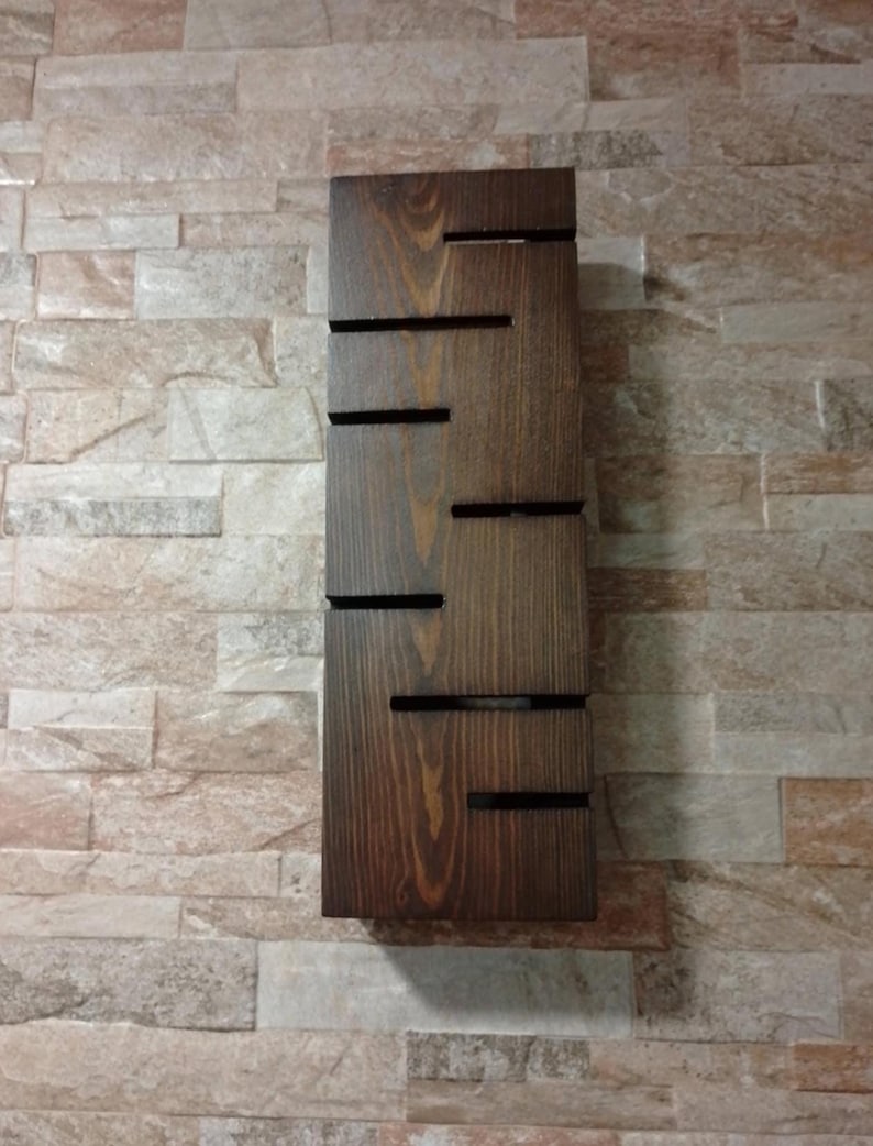 A rustic wooden wall sconce with warm glowing light. The lamp is carved with several horizontal slots that let the light escape in thin beams. The wood grain is visible and finished in a natural brown tone. A modern minimalist lighting piece suitable for living rooms, bedrooms, or entryway decor.