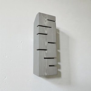 A vertical rectangular wooden wall sconce with warm LED light shining through carved horizontal openings. The wood has a natural grain and rustic brown finish. The style is minimalist, cozy, and modern, suitable for hallway, living room, or bedroom wall lighting.