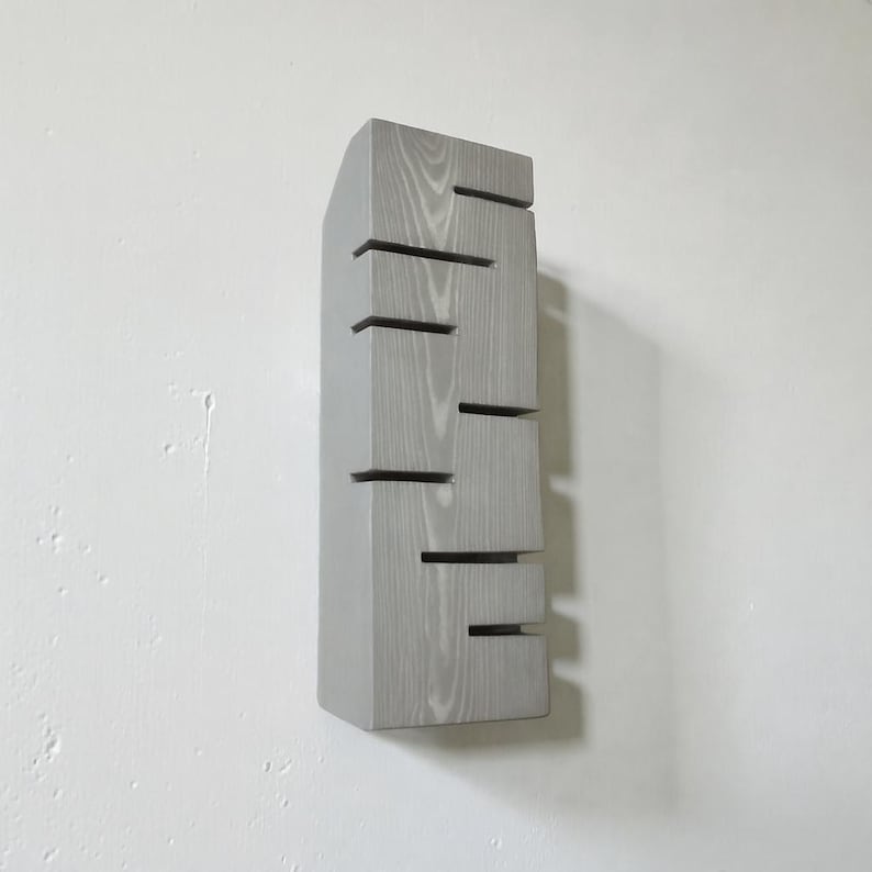 A vertical rectangular wooden wall sconce with warm LED light shining through carved horizontal openings. The wood has a natural grain and rustic brown finish. The style is minimalist, cozy, and modern, suitable for hallway, living room, or bedroom wall lighting.
