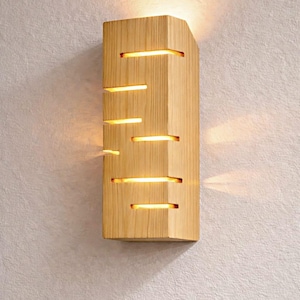 A vertical rectangular wooden wall sconce with warm LED light shining through carved horizontal openings. The wood has a natural grain and rustic brown finish. The style is minimalist, cozy, and modern, suitable for hallway, living room, or bedroom wall lighting.
