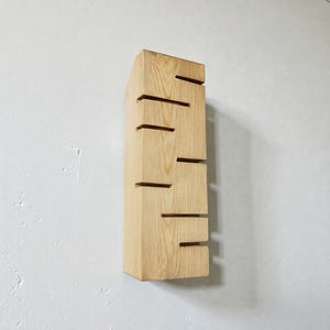 A vertical rectangular wooden wall sconce with warm LED light shining through carved horizontal openings. The wood has a natural grain and rustic brown finish. The style is minimalist, cozy, and modern, suitable for hallway, living room, or bedroom wall lighting.
